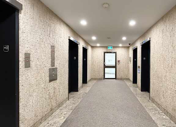 A long hallway with doors on both sides and a light green exit sign above the doors.