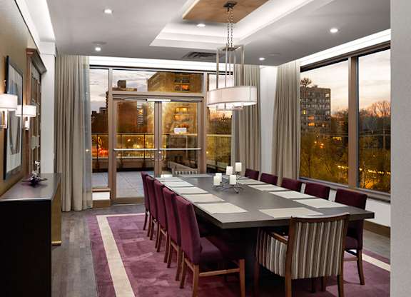 A long table with chairs is set up in a room with a view of the city.