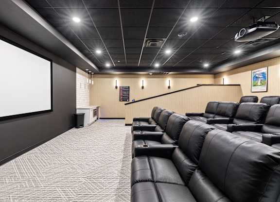 A modern home theater with black leather seats and a large screen.