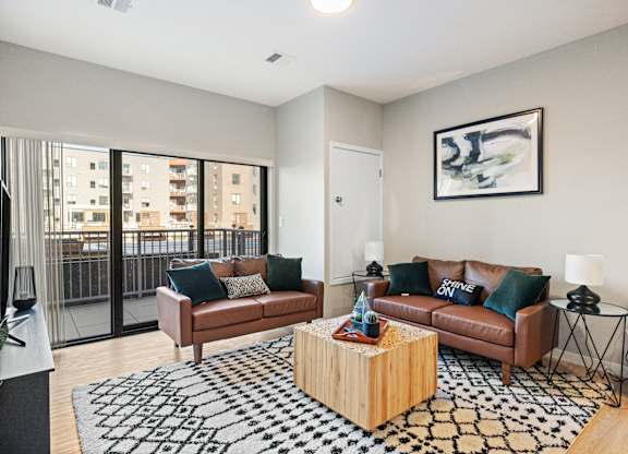 A living room with a brown couch, a black and white rug, and a painting on the wall.