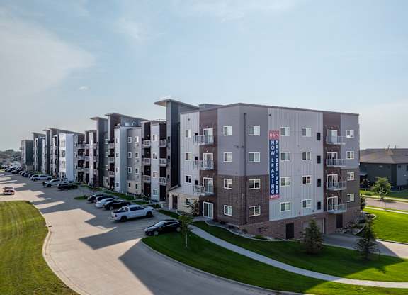 A row of apartment buildings with cars parked in front.