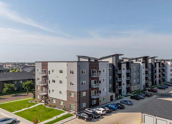 A row of apartment buildings with cars parked in the driveways.