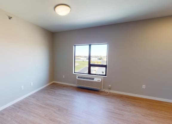 an empty living room with a window and wood floors at Northern Lights a Lifestyle-Driven Community, West Fargo, ND