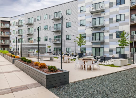 an open courtyard with tables and chairs in front of an apartment buildingat Northern Lights a Lifestyle-Driven Community, West Fargo, 58078