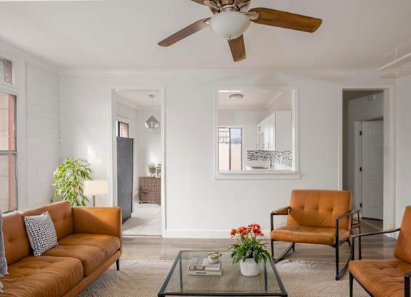 A living room with a brown sofa, two chairs, and a glass coffee table at Mariposa Willows Apartments, Los Angeles, California