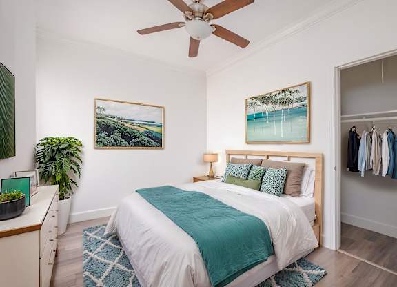 A bedroom with a bed, a ceiling fan, and a painting of a beach scene at Mariposa Willows Apartments, Los Angeles, CA
