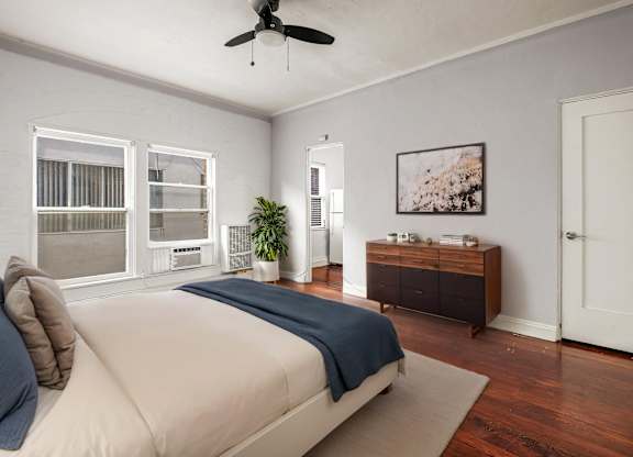 A bedroom with a bed, a ceiling fan, and a wooden cabinet.at Normandie Summit Apartments, Los Angeles, CA, 90004