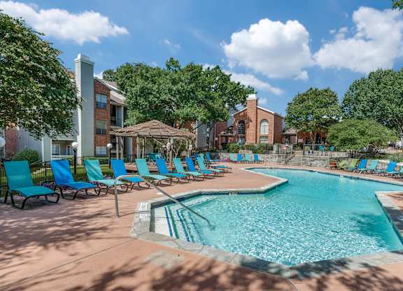 a resort style swimming pool with blue chairs and a building in the background at Foxborough Apartments, Irving, TX, Texas, 75061