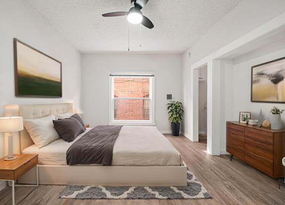 A bedroom with a large bed, a ceiling fan, and a window with a view of a red building at Hillstone Flats Apartments, Los Angeles, 90004