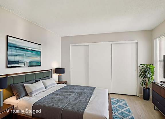A bedroom with a bed, a painting, a lamp, a plant, and a TV.