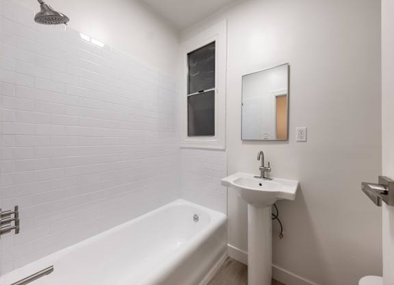 A white bathroom with a tub, sink, and mirror at Kenmore Park Apartments, Los Angeles, 90004