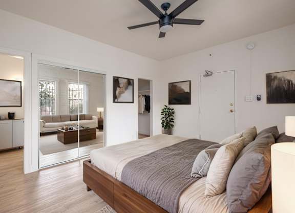 A bedroom with a bed, a ceiling fan, and a mirrored doorway leading to a living room at Kenmore Park Apartments, Los Angeles, 90004