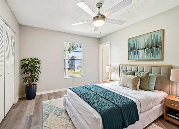 A bedroom with a bed, a ceiling fan, and a potted plant.