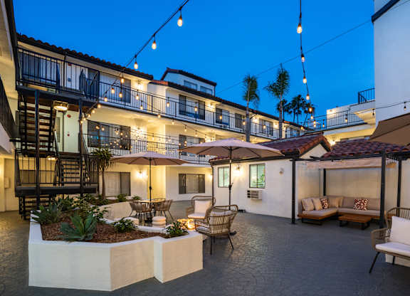 a courtyard with tables and chairs and umbrellas at night