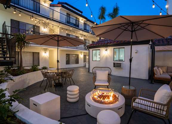 a patio with a fire pit and chairs and umbrellas