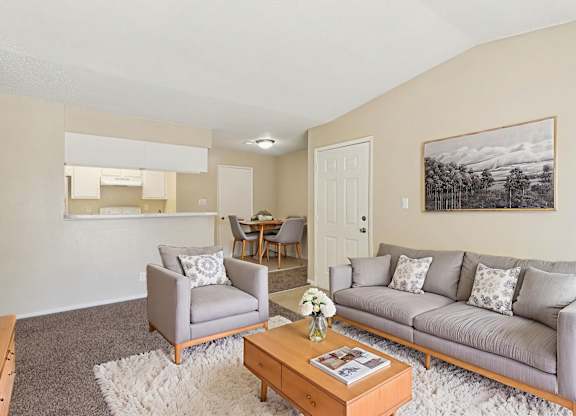 A living room with a grey couch, a grey armchair, a coffee table, and a painting on the wall.