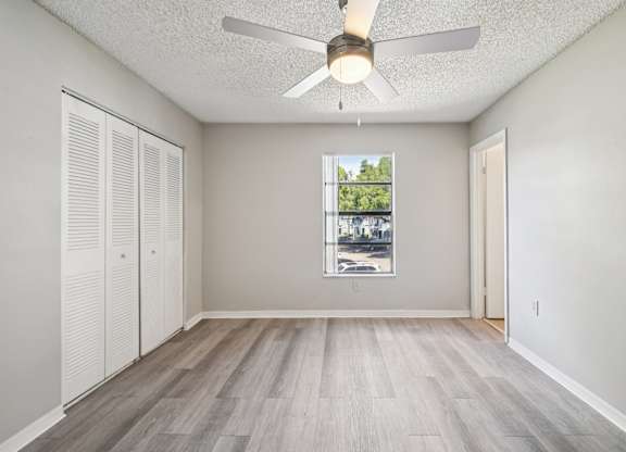 A room with a ceiling fan and a window showing a view of trees and buildings outside.