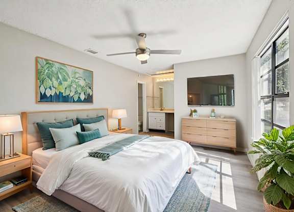 A bedroom with a large bed, a ceiling fan, and a painting on the wall.