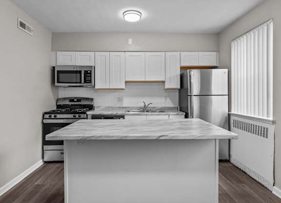 an empty kitchen with white cabinets and stainless steel appliances and a marble counter top at Hampton Gardens, Missouri, 63139