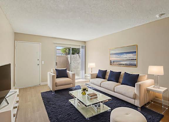 A living room with a white couch, a glass coffee table, and a painting on the wall.