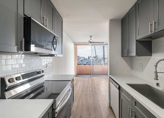 A modern kitchen with a stove top oven, microwave, and a sink.at Menlo Terrace Apartments, Los Angeles, California