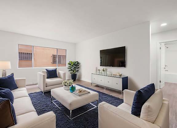 A living room with a white sofa, a white coffee table, and a TV on the wall.