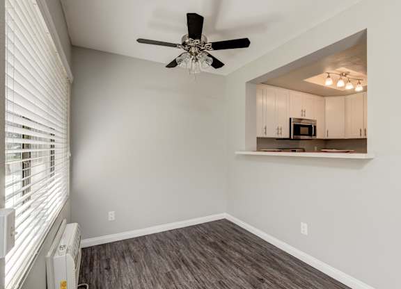 an empty living room with a ceiling fan and a kitchen