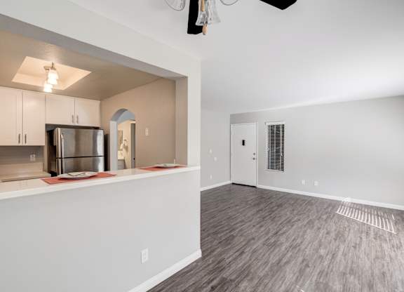 the living room and kitchen of an apartment with white walls and wood flooring