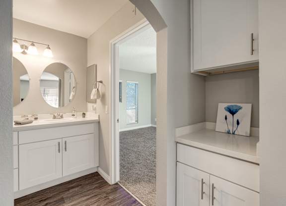 a kitchen with white cabinets and a mirror and a door to a hallway
