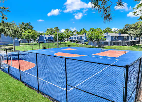 A blue tennis court surrounded by a black fence.