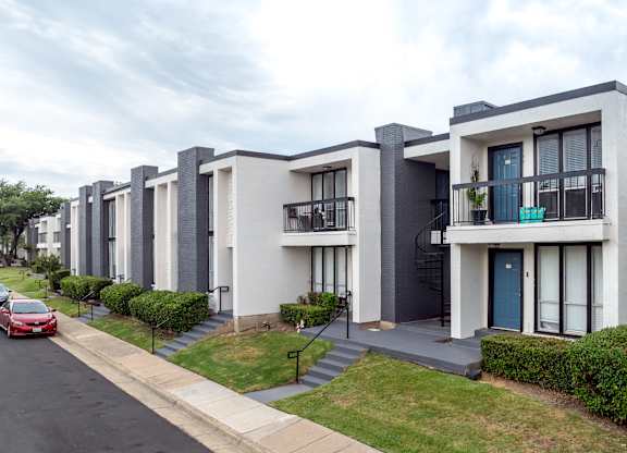 A red car is parked on the street in front of a row of townhouses.