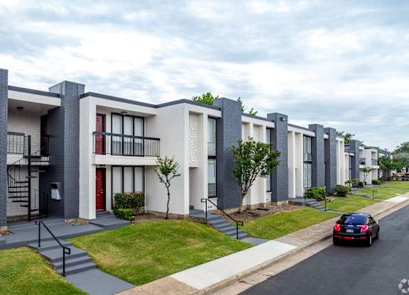 A black car is driving down a street lined with modern apartment buildings.
