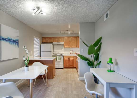A white table with a vase of flowers on it sits in a kitchen with a white fridge and wooden cabinets.