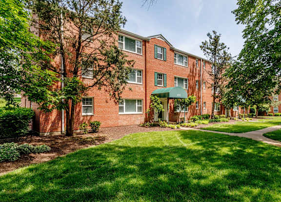 exterior view of a brick apartment building with green grass and trees at Hampton Gardens, Missouri, 63139
