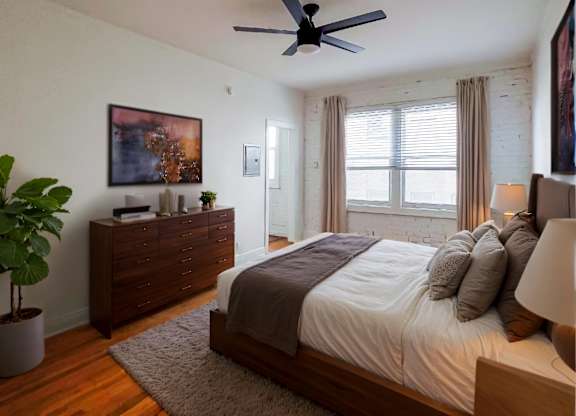 A bedroom with a bed, dresser, and ceiling fan at Kenmore Park Apartments, California