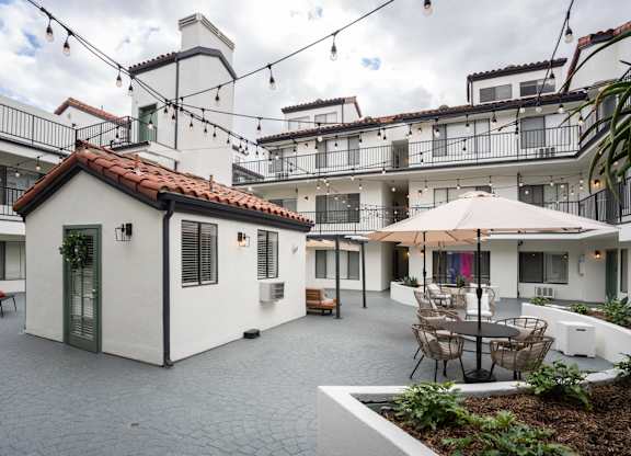 the courtyard of a white apartment building with tables and chairs