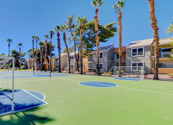 A basketball court surrounded by palm trees and apartment buildings.