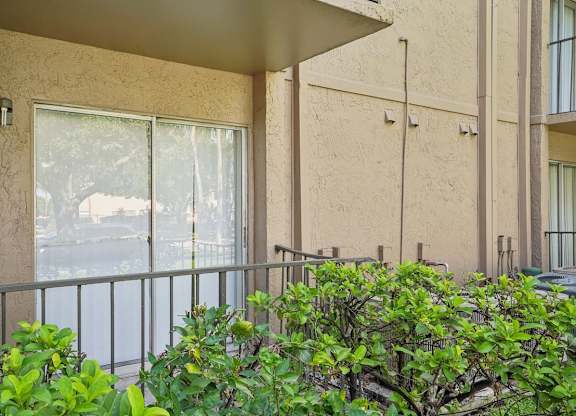 A balcony with a metal railing and bushes in front.