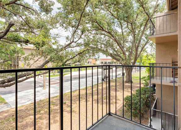A balcony with a black railing overlooks a tree-lined street.