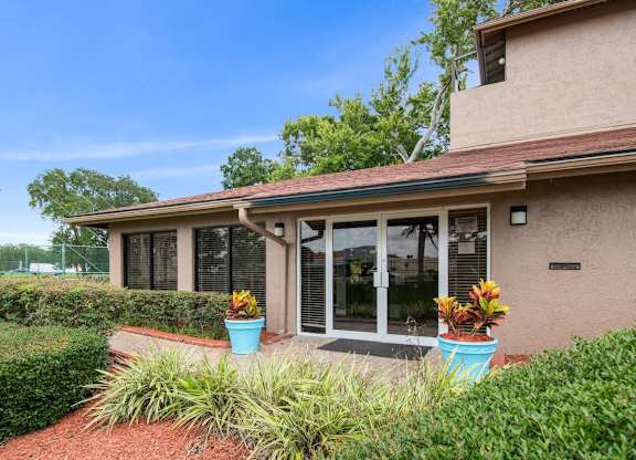 A house with a brown roof and a glass door is surrounded by green plants.