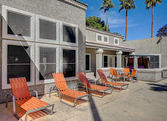 A patio with orange chairs and a grey building.
