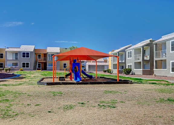 A playground with a red canopy and a blue slide in the middle of a grassy area.
