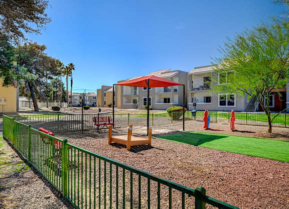 A playground with a green fence and a red umbrella.