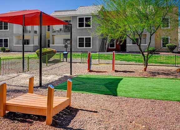 A playground with a red umbrella and a wooden bench.