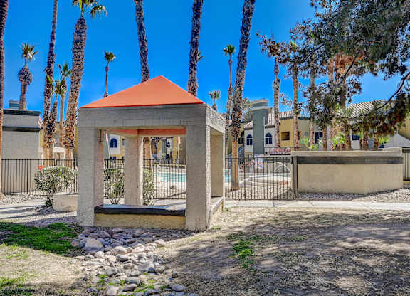 A gazebo with a red roof is surrounded by palm trees.