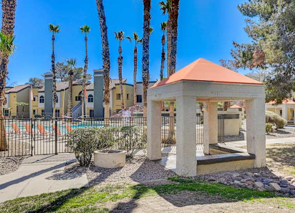 A gazebo-like structure sits in the middle of a courtyard with palm trees in the background.