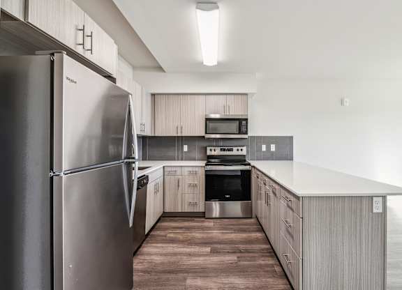 A modern kitchen with a stainless steel refrigerator and wooden flooring.