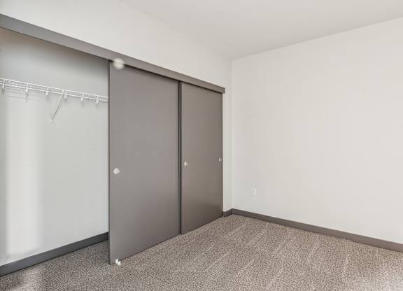 A room with a grey carpet and a grey wardrobe with a white coat hanger.