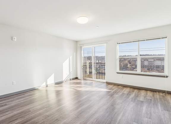 A spacious room with wooden floors and a view of the city through the windows.