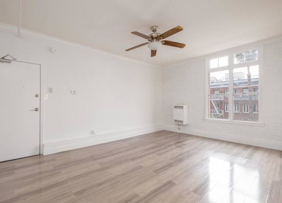 A room with a ceiling fan and a window showing a view of a building outside at Mariposa Willows Apartments, California